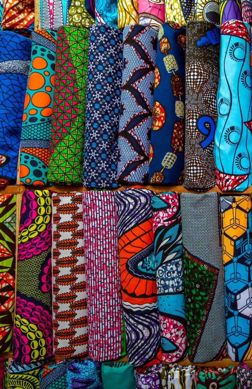 Stacked bolts of wax-print cloth in blue, ochre and green